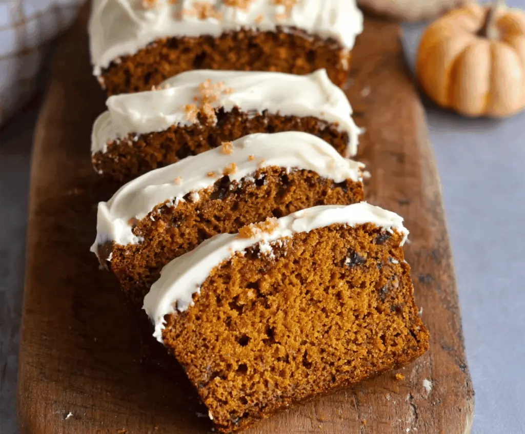 Homemade pumpkin bread topped with creamy cream cheese frosting on a rustic platter, featuring fresh pumpkin and cinnamon for a cozy fall treat.
