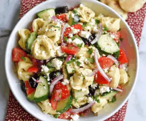 Colorful Greek Tortellini Pasta Salad with cherry tomatoes, cucumbers, olives, feta cheese, and fresh herbs in a bowl, perfect for summer picnics and parties.