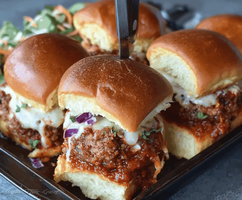 Delicious meatloaf sliders topped with melted cheese and fresh herbs on a serving platter.