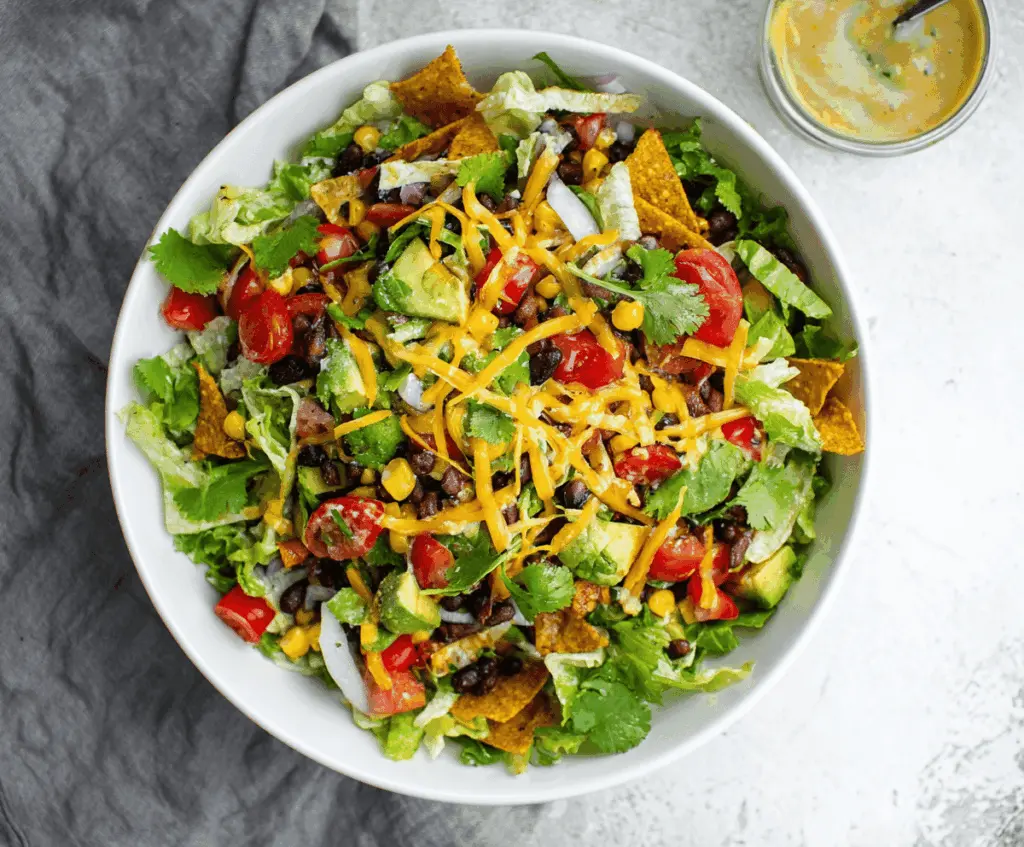 Colorful vegetarian black bean taco salad with fresh vegetables, crispy tortilla chips, and melted cheese in a vibrant bowl
